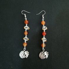 Silver plated chainmaille in a variation of butterfly weave, studded with orange glass seed beads, mirrors the shape of the focal points, two pumpkin charms. Round carnelian beads in varying shades of orange bring to mind the squash's vibrant colour. An ideal Halloween gift or autumnal accessory. Each earring is approximately 4.25 inches (10.6 cm) in length, with a drop length of 3.5 inches (8.7 cm). Orange Jewelry With Silver Beads As A Gift, Orange Jewelry With Silver Beads For Gift, Orange Beaded Czech Glass Jewelry, Orange Sterling Silver Jewelry With Round Beads, Handmade Carnelian Orange Earrings, Handmade Orange Carnelian Earrings, Nickel Free Carnelian Orange Earrings, Adjustable Orange Metal Jewelry, Adjustable Nickel-free Carnelian Jewelry