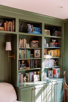 a green bookcase filled with lots of books next to a white chair and lamp