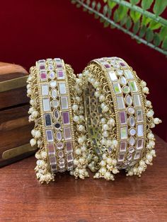 This authentic Kalinda bangle is a classic blend of traditional aesthetics and modern craftsmanship. Intricately crafted of brass with real mirror and pearl work, its one-inch width and champagne stone sparkle make it a chic, timeless addition to any ensemble. Comes in a pair. Pearl Work, Kundan Bangles, One Inch, Champagne, Bangles, Sparkle, Brass, Mirror, Stone