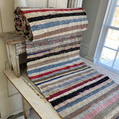 a multicolored rag rug sitting on top of a wooden bench next to a window