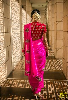 a woman in a pink sari walks down a hallway with her back turned to the camera