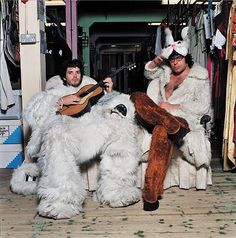 two men dressed in furry costumes are playing guitar and singing while sitting on the floor