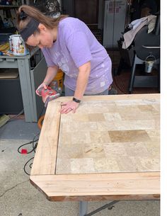 a woman sanding wood on top of a table with a power drill in her hand