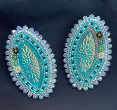 two blue and green beaded earrings on a black surface with beads around the edges