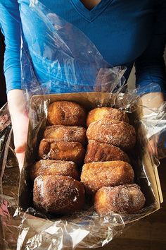 a box filled with donuts sitting on top of a table next to a woman