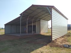 a man standing in the doorway of a metal building under a large awning on top of a grass covered field