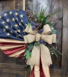 a wreath with an american flag and evergreens on it hanging from a wooden door