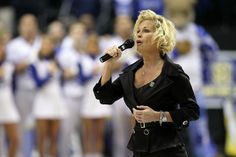 a woman singing into a microphone in front of a group of women on the sidelines