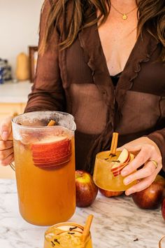 a woman sitting at a table with two glasses filled with apple cider and cinnamon sticks