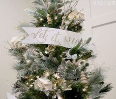 a christmas tree decorated with silver and white ornaments, bows and ribbon that says let it snow