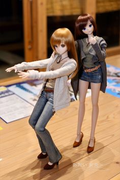 two dolls are posed in front of a wooden floor and one is pointing at something