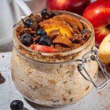 a glass jar filled with oatmeal sitting next to apples and blueberries