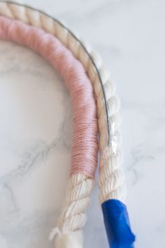 a close up of a rope with a blue handle on a marble surface, next to a pink and white cord