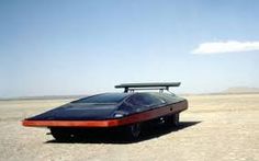 a black car with a surfboard on the roof is parked in an empty desert