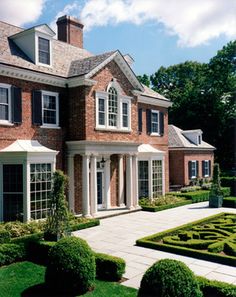 a large brick house surrounded by hedges and trimmed with boxwood trees in the front yard