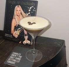 a martini glass sitting on top of a table next to a book about cocktails