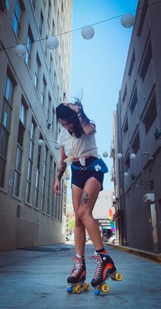 a woman riding on top of a skateboard down a street next to tall buildings