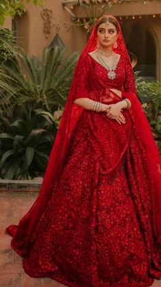 a woman in a red wedding gown standing on a brick floor with greenery behind her