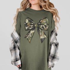 This stylish camoflauge bow t-shirt is the perfect blend of edgy and feminine fashion. The unique camoflauge print adds a touch of military-inspired trendiness, while the bow detail on the front brings a cute and playful touch. Made from soft and comfortable fabric, this t-shirt is ideal for everyday wear or for adding a statement piece to your outfit. Stand out from the crowd with this eye-catching camoflauge bow t-shirt! SIZE UP 1-2 SIZES FOR AN OVERSIZED LOOK! Thanks so much for shopping with Camouflage T-shirt For Fall, Fall Camouflage T-shirt With Crew Neck, Fall Camouflage Crew Neck T-shirt, Fall Camouflage Tops With Graphic Print, Fall Cotton Top With Bow Detail, Army Wife, Military Wife, Military Inspired, Feminine Style