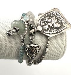 "Handmade Boho Bracelets featuring a Vintage Hindu Durga Warrior Goddess Silver Charm (about 1 1/2\" x 7/8\") pairs with small faceted Gray and Cloudy Quartz beads.  There is a 925 Sterling Silver Embossed Button that serves as the clasp, added to the set is a small Aqua glass beaded bracelet with an Aventurine Bead clasp.  Last is small silver tone beads with coordinating Aqua colored beads.  The set is charming, unique and perfect for the Warrior Woman in us all. Specifics ✥ Small Green Bracel Adjustable Silver Beads Jewelry With Unique Style, Adjustable Silver Wrap Bracelet With Natural Stones, Silver Wrap Bracelet With Round Natural Stones, Elegant Silver Stretch Bracelet For Healing, Silver Spiritual Stretch Bracelet Stackable, Bohemian Silver Stretch Bracelet With Silver Beads, Silver Hand-strung Jewelry As A Gift, Silver Hand-strung Jewelry For Gifts, Adjustable Nickel-free Silver Crystal Bracelet