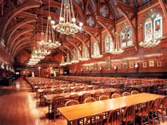 a large room with wooden tables and chairs in front of chandeliers hanging from the ceiling