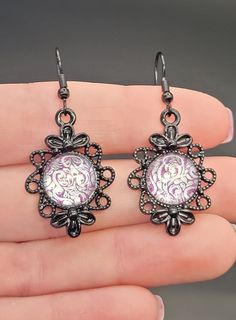 The design in these earrings was hand created with nail polish!  This pair features a glittery magenta base with a silver design.  The design is set with glass in a black tone floral metal base, and features hypoallergenic stainless steel ear wires. Inner Diameter/Design Size: 12mm Outside Diameter: 20mmx30mm Total Length with Ear Wire: 50mm Silver Design, Metal Base, Ear Wire, Ear Wires, Jewelry Earrings Dangle, Dangle Drop Earrings, Dangle Earrings, Nail Polish, Jewelry Earrings