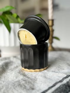 a black and white container with some cream in it sitting on a table next to a potted plant