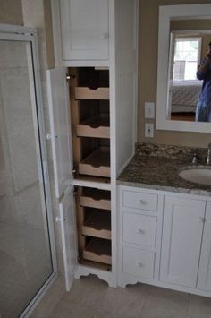 a person taking a photo of a bathroom with white cabinets and marble counter tops, in front of a large mirror