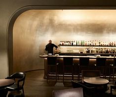 a man standing behind a bar with lots of bottles on the shelves and stools