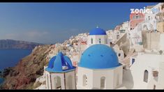 there are many white and blue buildings on the cliff side with water in the background