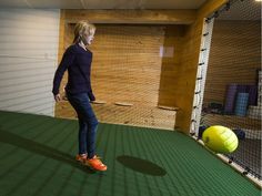 a woman standing on top of a green floor next to a soccer ball in a room