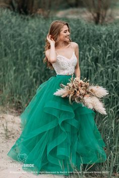 a woman in a green dress is standing by some tall grass and holding a bouquet