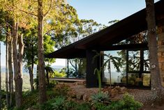 the house is surrounded by trees and plants in front of some rocks on the ground