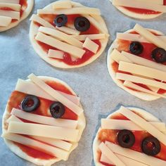 four pizzas with cheese and olives on them are arranged in the shape of faces