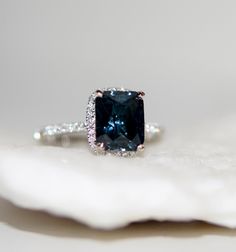 a blue diamond ring sitting on top of a white piece of paper with diamonds around it