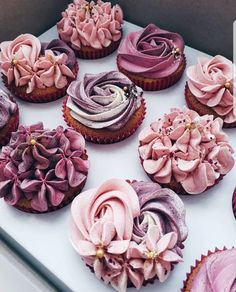 cupcakes decorated with pink and purple frosting on a white tablecloth in a box