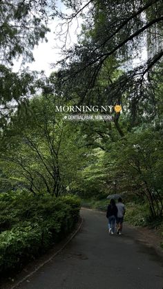 two people walking down a path in the middle of a park with trees and bushes