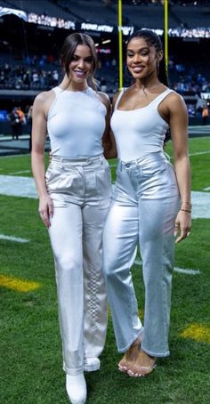 two women standing next to each other on top of a field at a football game