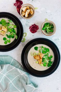 two black bowls filled with soup and garnished with green leafy toppings