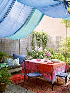 an outdoor dining area is decorated with blue and pink decor, including curtains over the table