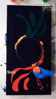 a person in blue gloves is painting on a black piece of paper with orange and red paint