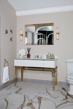 a bathroom with a marble floor and white vanity, gold mirror over the sink and toilet