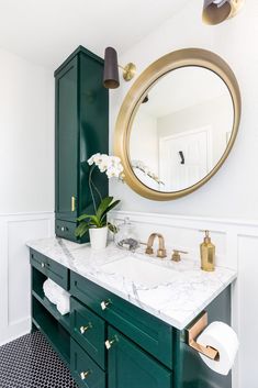 a bathroom with green cabinetry and marble counter top, gold mirror above the sink