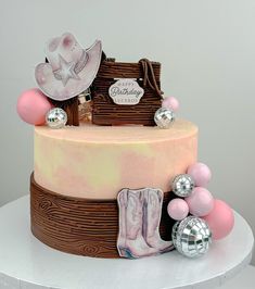 a pink and brown birthday cake with cowboy boots, balloons, and confetti