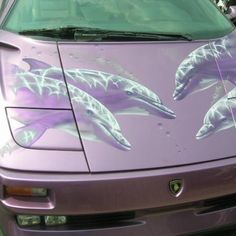 two dolphins painted on the hood of a purple sports car in front of some parked cars