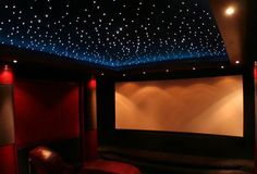 a home theater with stars on the ceiling and red chairs in front of the screen