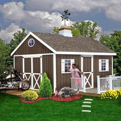 a woman standing in front of a brown and white shed with a motorcycle parked next to it