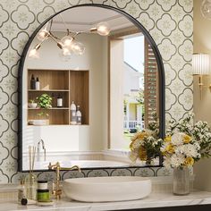 a bathroom sink sitting under a large mirror next to a bathtub and vase with flowers