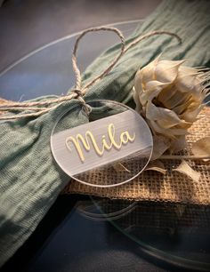 a glass plate topped with a wooden name tag next to a flower on top of burlap