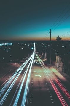 an aerial view of the city at night with light streaks on the road and power lines above